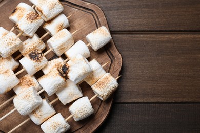 Photo of Sticks with roasted marshmallows on wooden table, top view. Space for text