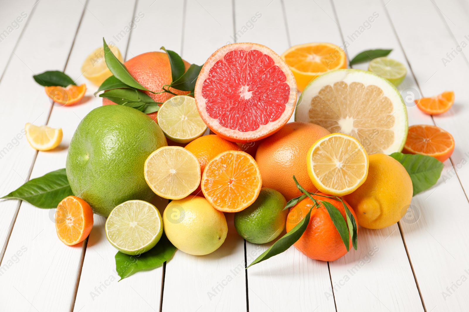 Photo of Different citrus fruits with fresh leaves on white wooden table