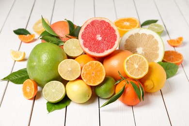 Different citrus fruits with fresh leaves on white wooden table