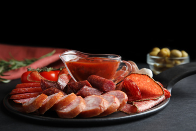 Photo of Different types of sausages with sauce served on black table