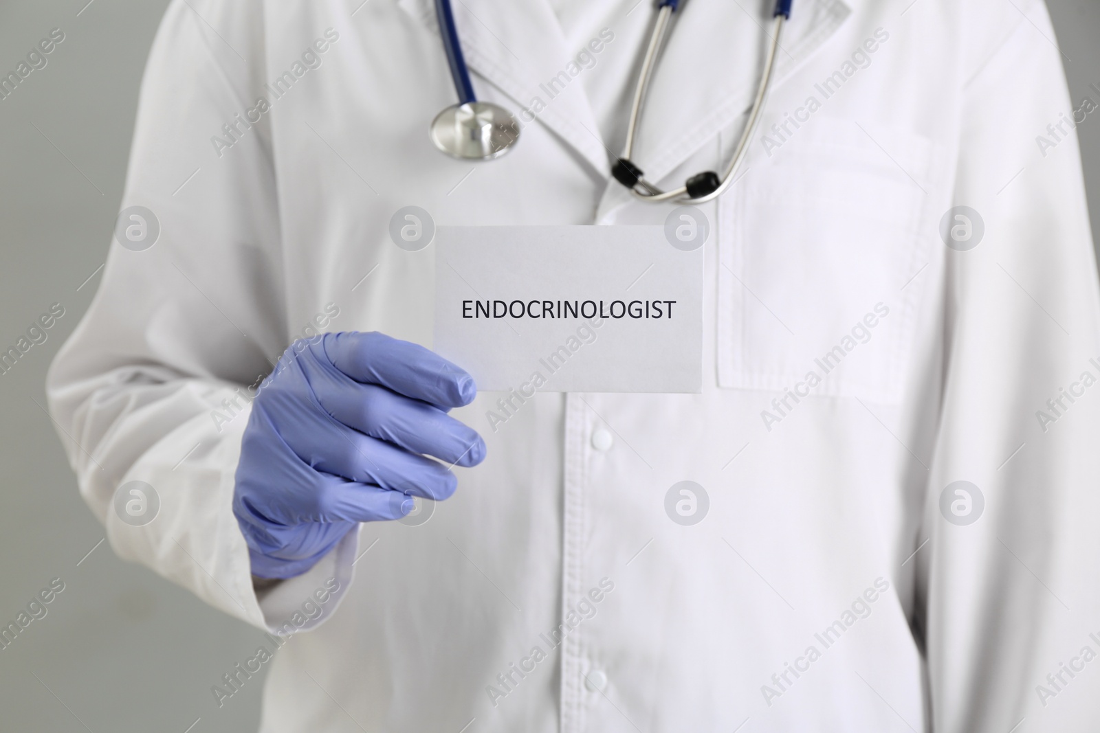 Image of Endocrinologist with stethoscope holding card on grey background, closeup