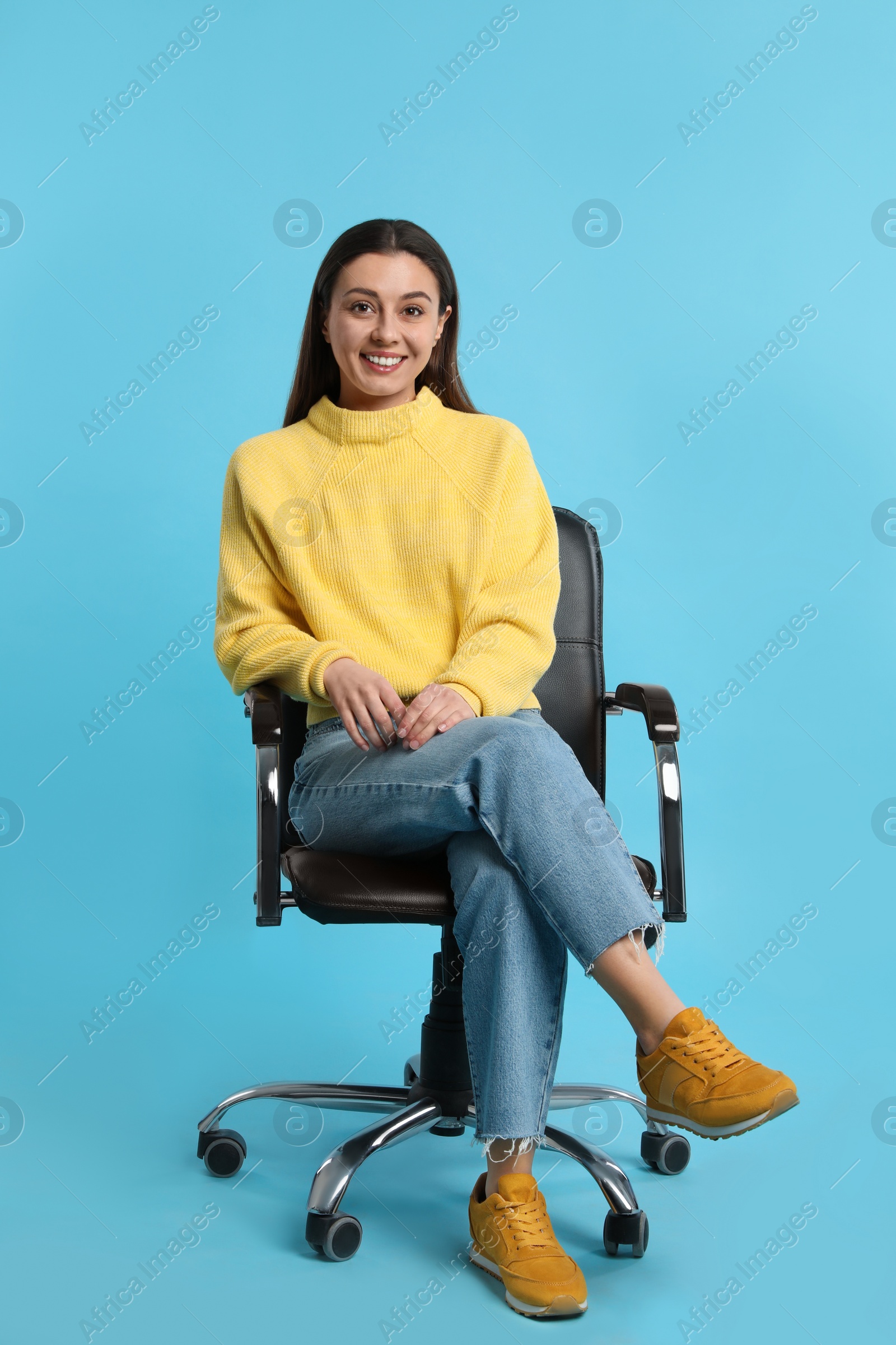 Photo of Young woman sitting in comfortable office chair on turquoise background