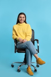 Young woman sitting in comfortable office chair on turquoise background