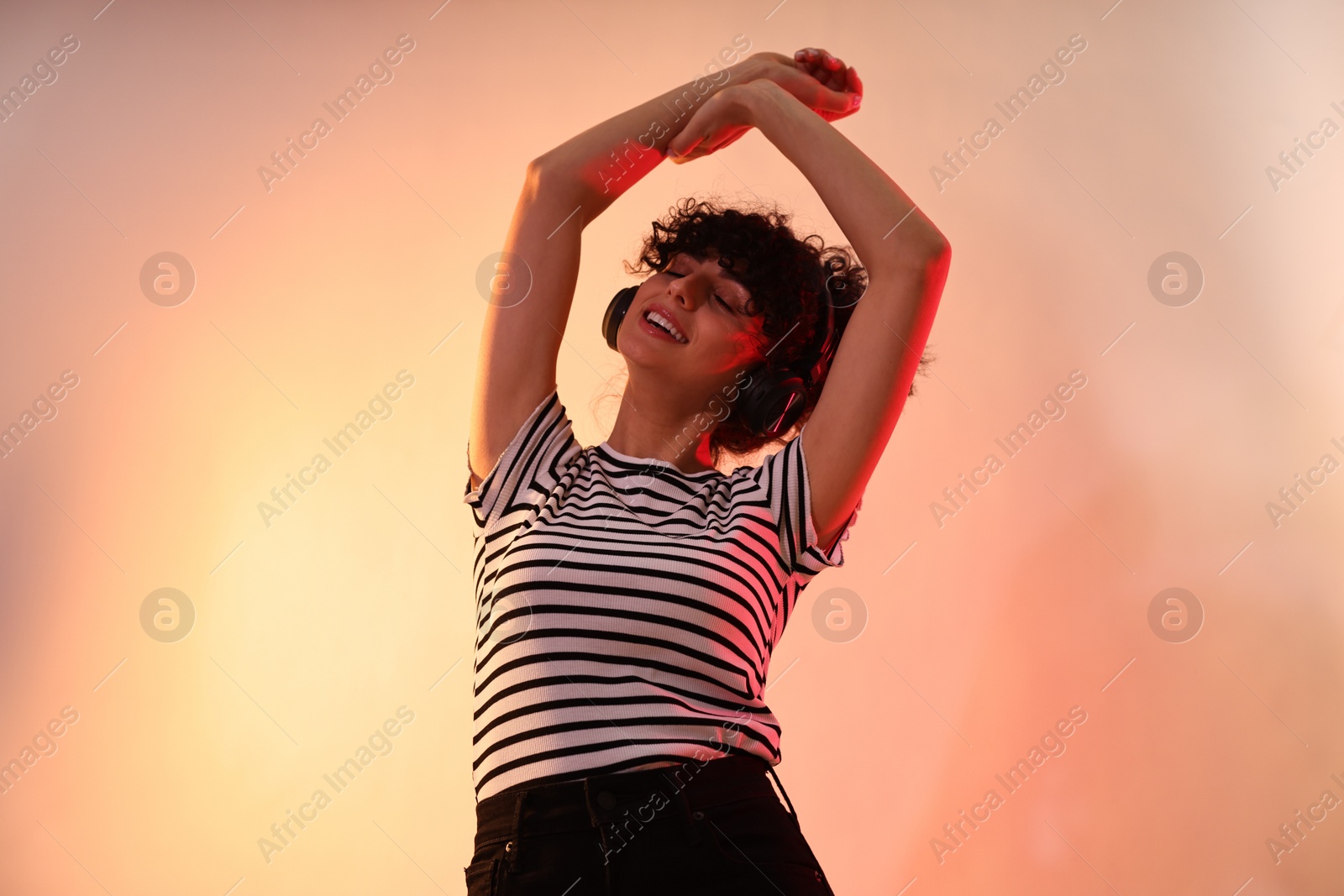 Photo of Beautiful young woman listening to music with headphones on color background in neon lights, low angle view