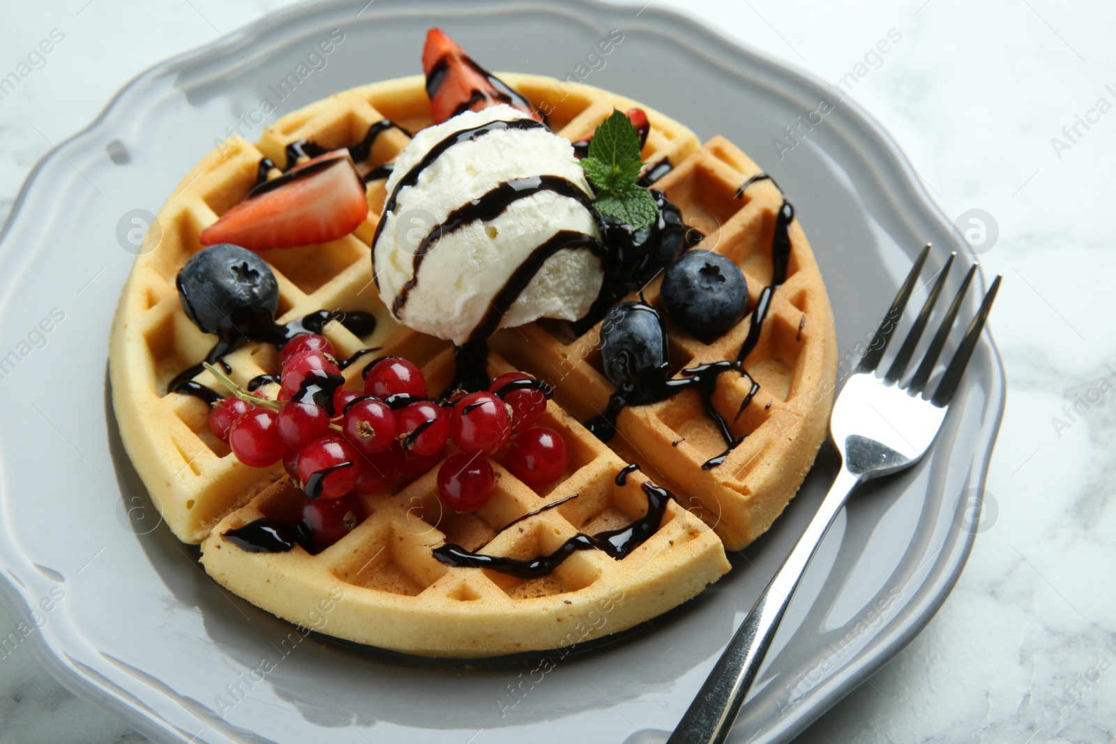 Photo of Delicious Belgian waffles with ice cream, berries and chocolate sauce on light marble table, closeup