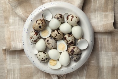 Unpeeled and peeled hard boiled quail eggs in bowl on white wooden table, top view