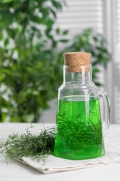 Photo of Jug of homemade refreshing tarragon drink and sprigs on white table