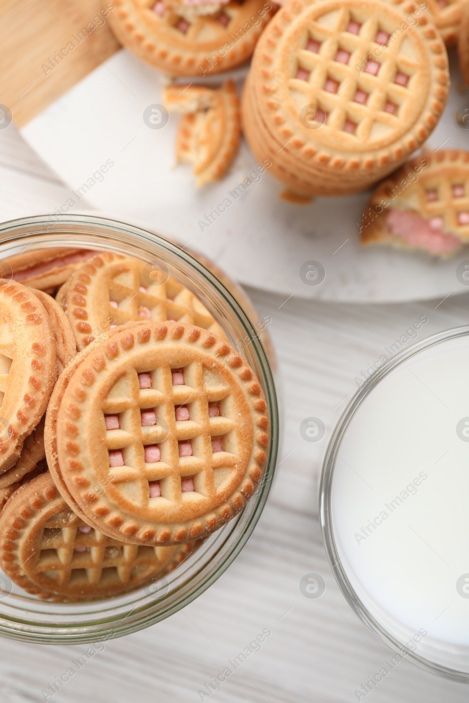 Photo of Tasty sandwich cookies with cream and glass of milk on white wooden table, flat lay