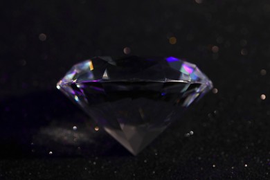 Photo of Beautiful dazzling diamond on black glitter surface, closeup