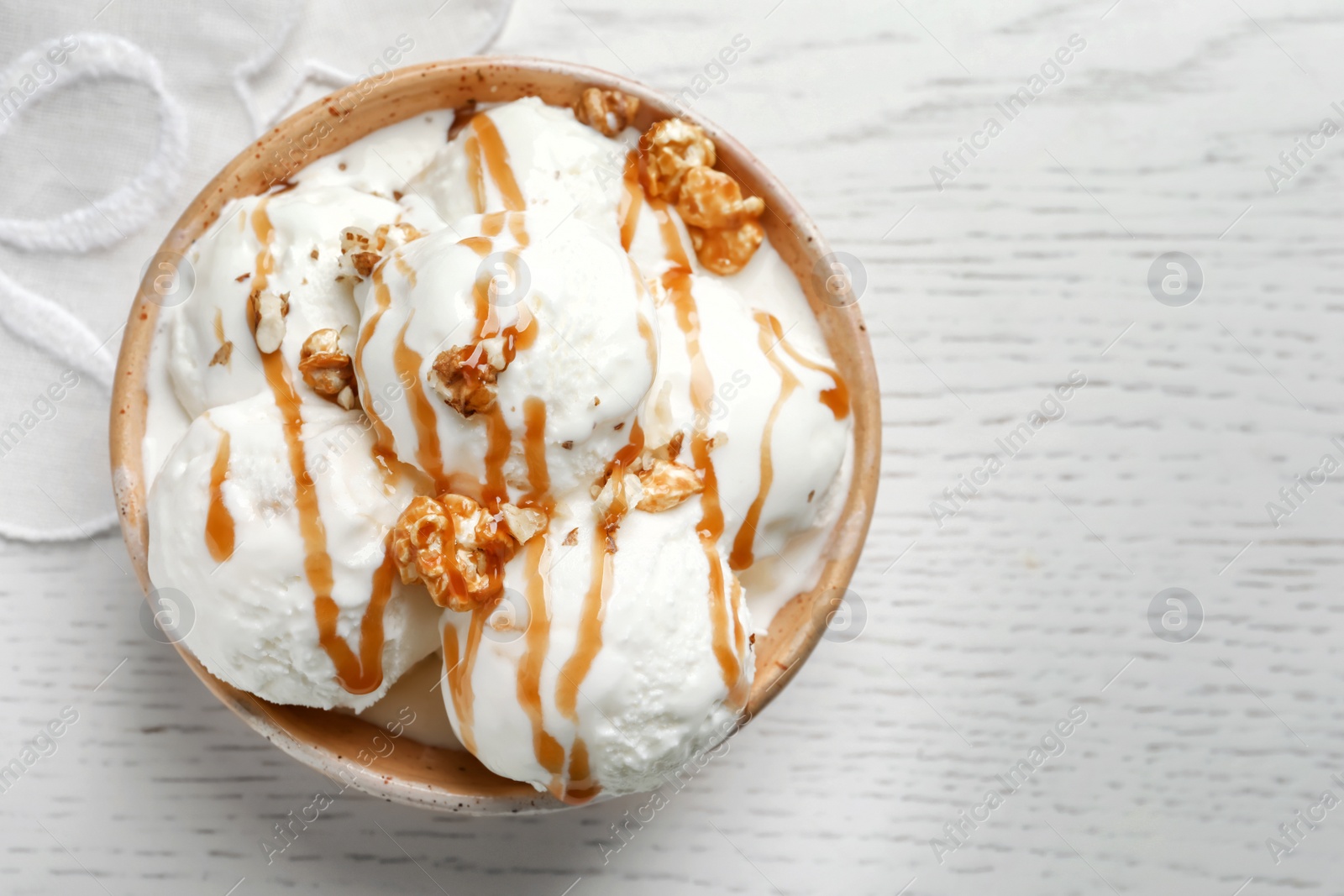 Photo of Tasty ice cream with caramel sauce and popcorn in bowl on table