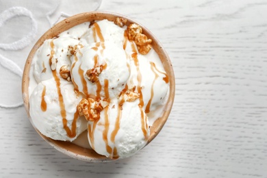 Tasty ice cream with caramel sauce and popcorn in bowl on table