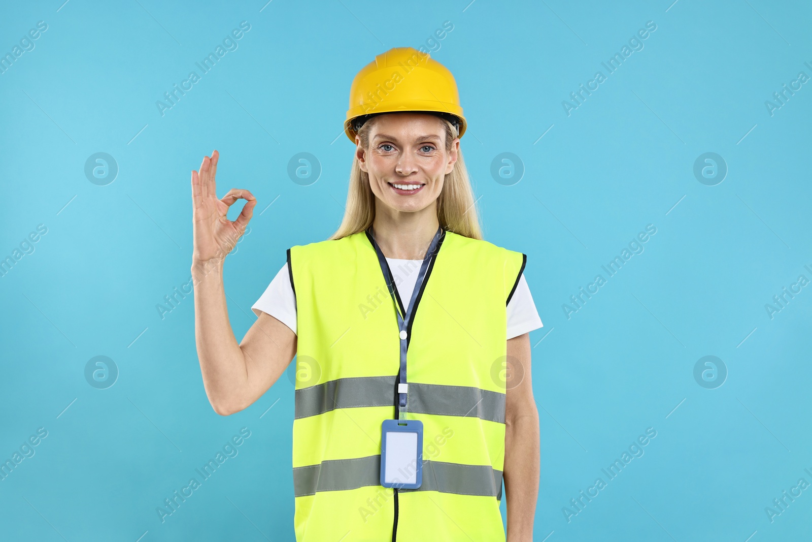 Photo of Engineer with hard hat and badge showing ok gesture on light blue background