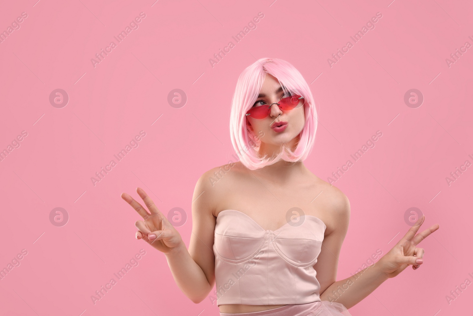 Photo of Pink look. Funny girl in wig and top wearing bright sunglasses on color background