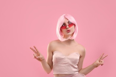 Photo of Pink look. Funny girl in wig and top wearing bright sunglasses on color background