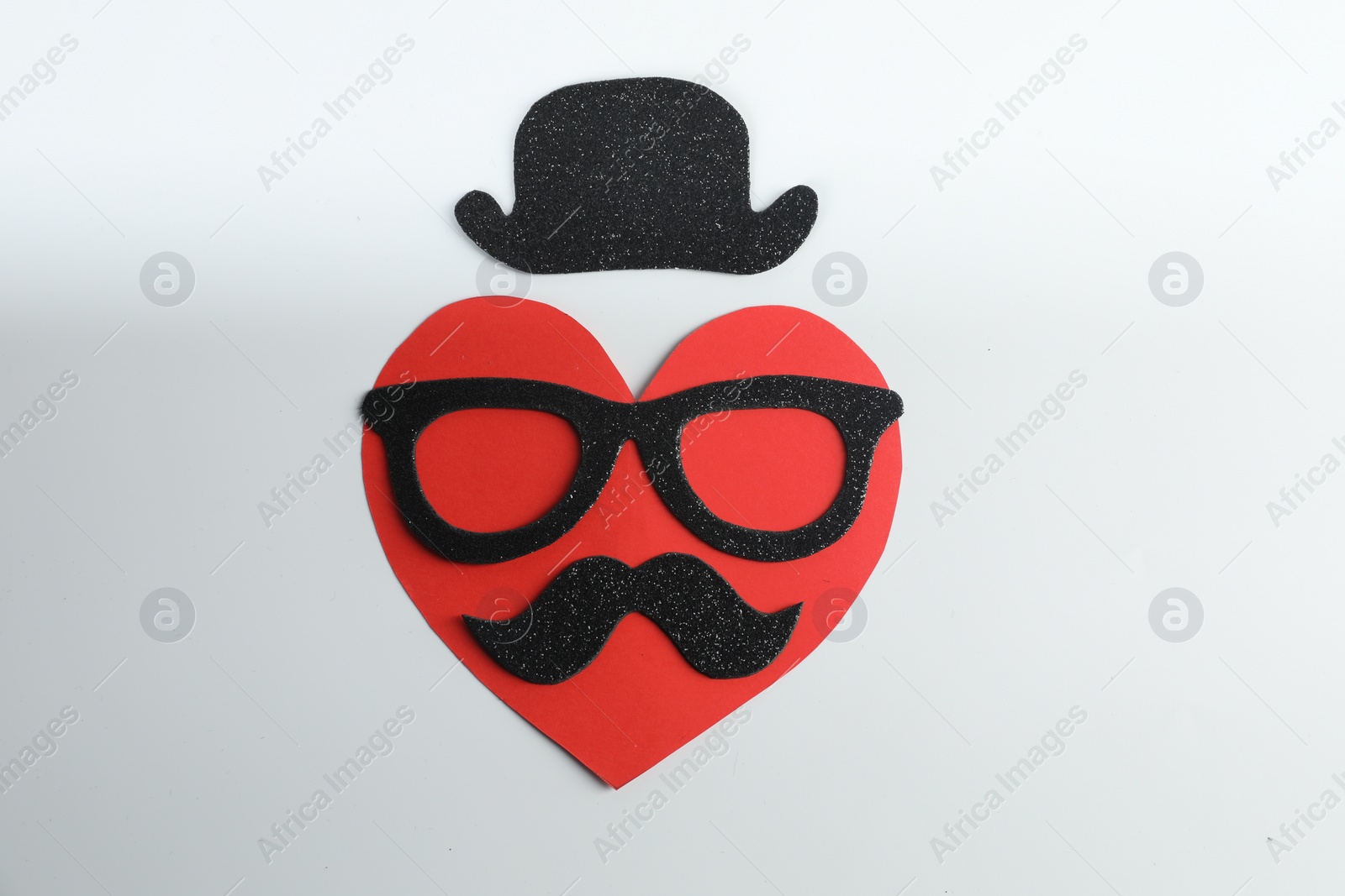 Photo of Man's face made of paper heart, fake mustache, glasses and hat on light background, top view