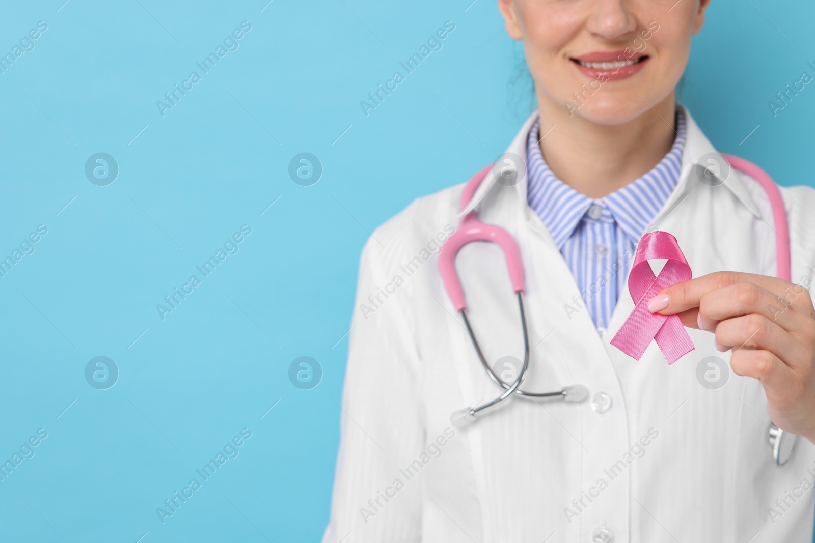 Photo of Breast cancer awareness. Mammologist with pink ribbon against light blue background, closeup. Space for text