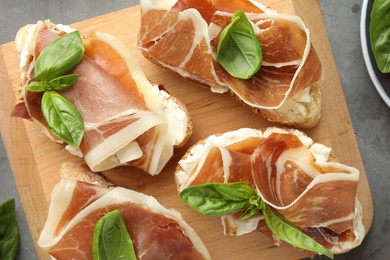 Photo of Tasty sandwiches with cured ham, tomatoes and arugula on grey table, top view