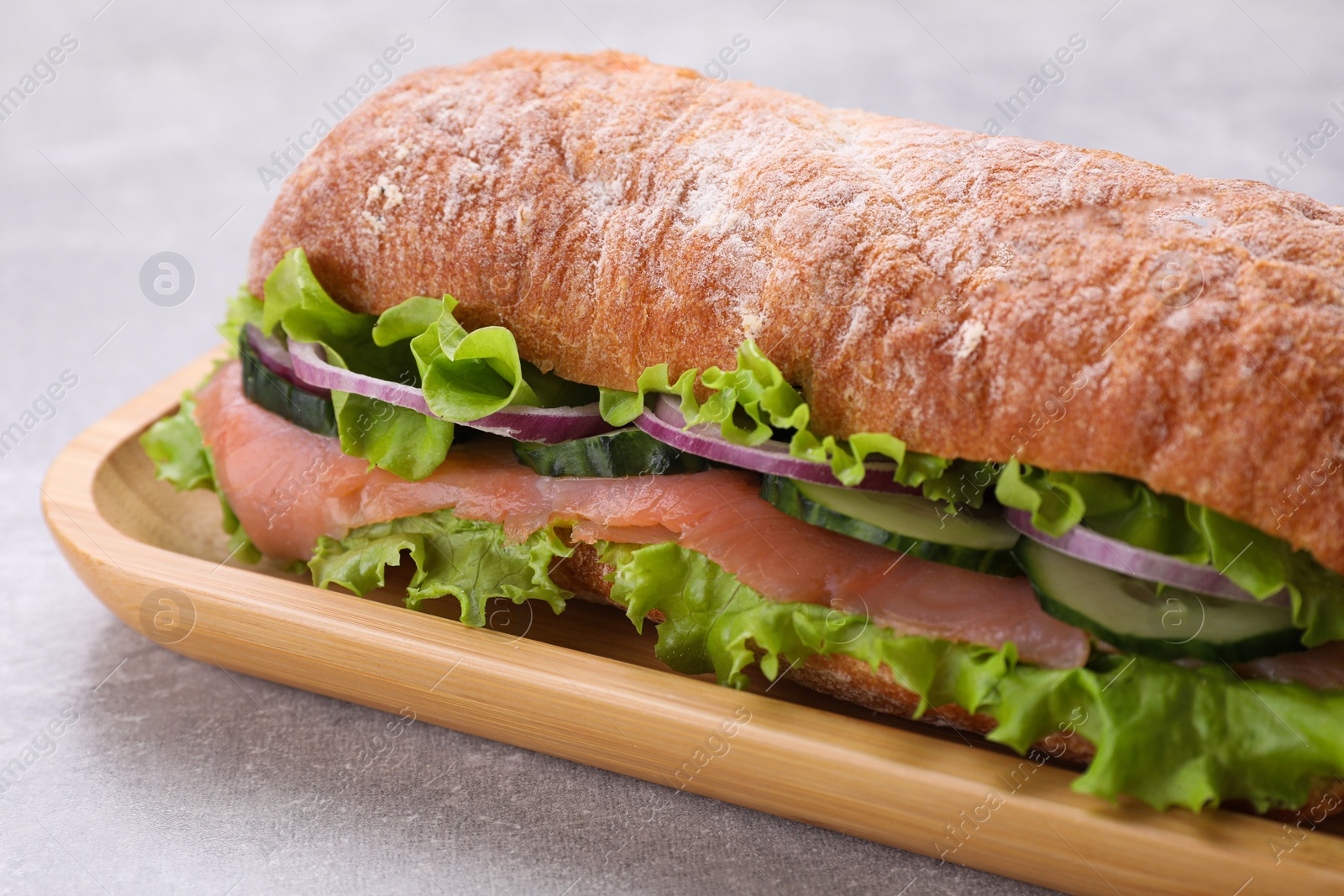 Photo of Delicious sandwich with fresh vegetables and salmon on light gray table, closeup