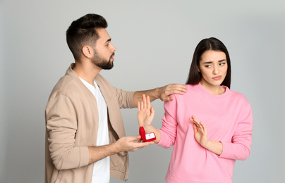 Young woman rejecting engagement ring from boyfriend on light grey background