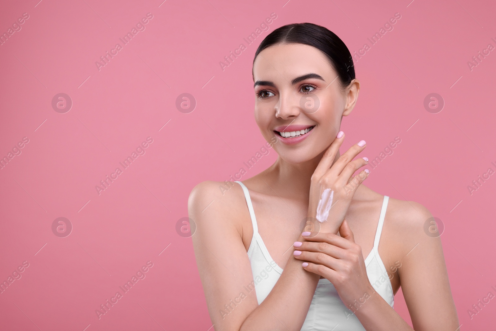 Photo of Beautiful woman with smear of body cream on her hand against pink background, space for text