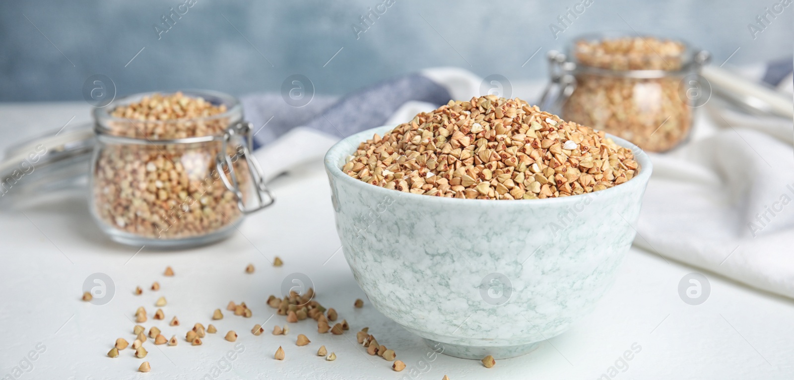 Image of Uncooked green buckwheat grains in bowl on white table. Banner design