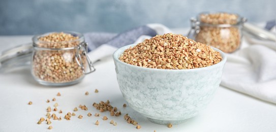 Image of Uncooked green buckwheat grains in bowl on white table. Banner design
