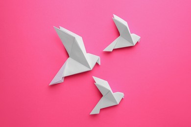 Photo of Beautiful white origami birds on pink background, flat lay