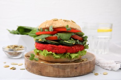 Photo of Tasty vegan burger with vegetables, patty and microgreens on white tiled table, closeup