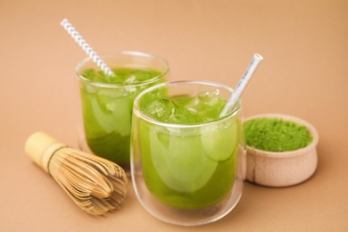 Delicious iced green matcha tea, powder and bamboo whisk on pale brown background, closeup