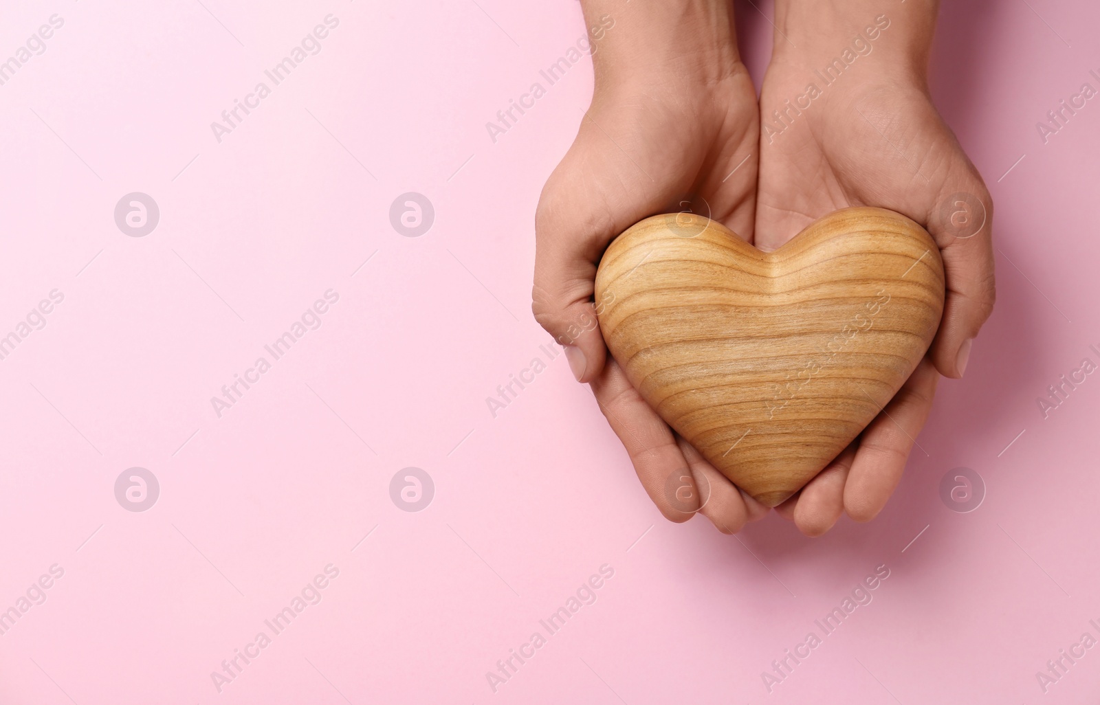 Photo of Woman holding wooden heart on pink background, top view. Space for text