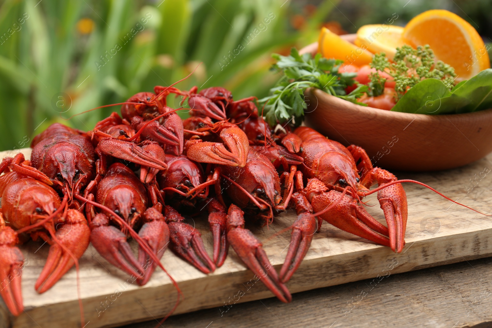 Photo of Delicious red boiled crayfish and products in bowl on wooden table