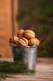 Photo of Metal bucket of delicious nut shaped cookies and fir branches on wooden table