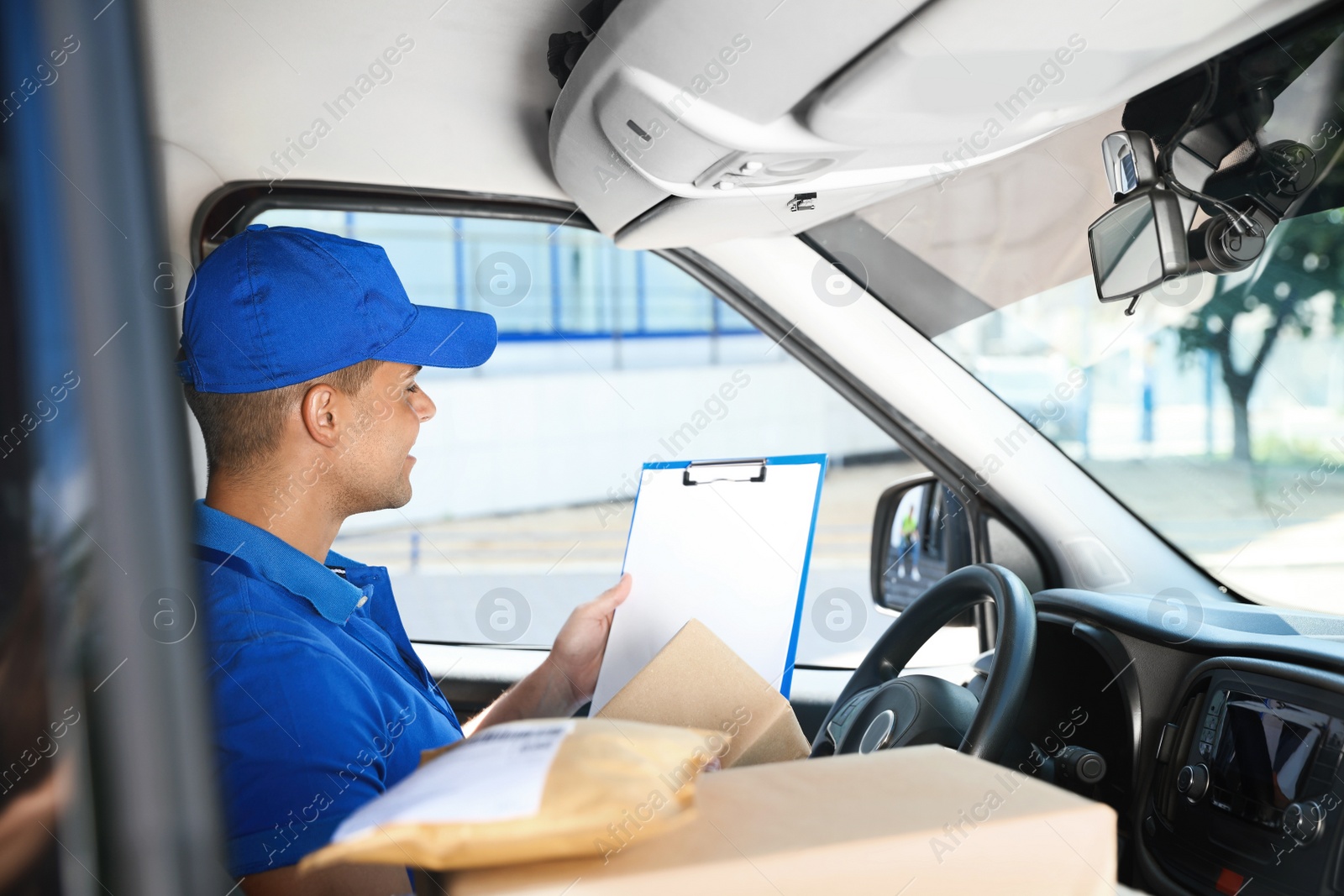 Photo of Young courier with clipboard and parcels in delivery car