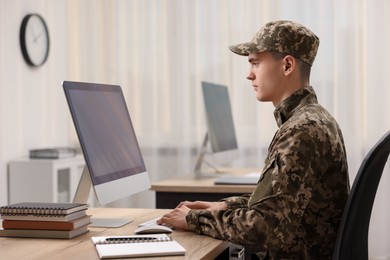 Photo of Military service. Young soldier working with computer at wooden table in office