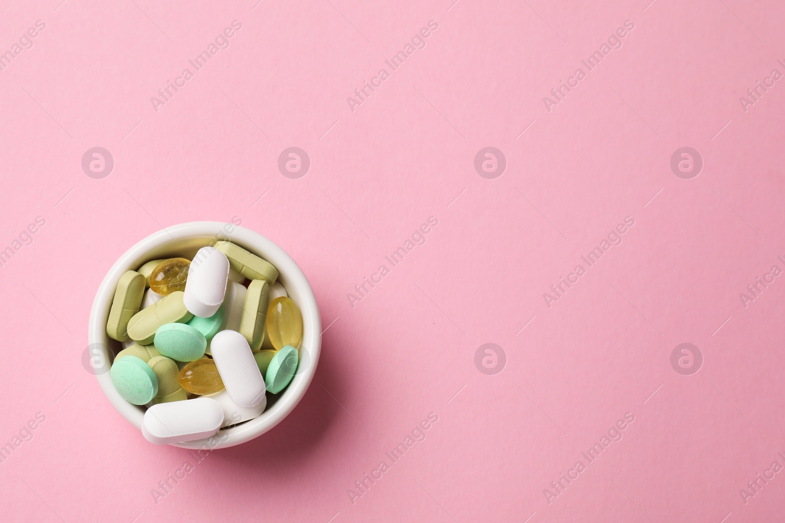 Photo of Different vitamin pills in bowl on pink background, top view. Space for text