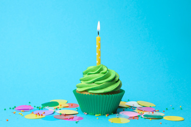 Delicious birthday cupcake with green cream and burning candle on light blue background