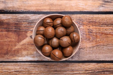 Photo of Delicious organic Macadamia nuts in bowl on wooden table, top view
