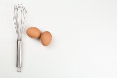 Photo of Raw eggs and whisk on white background, top view with space for text. Baking pie