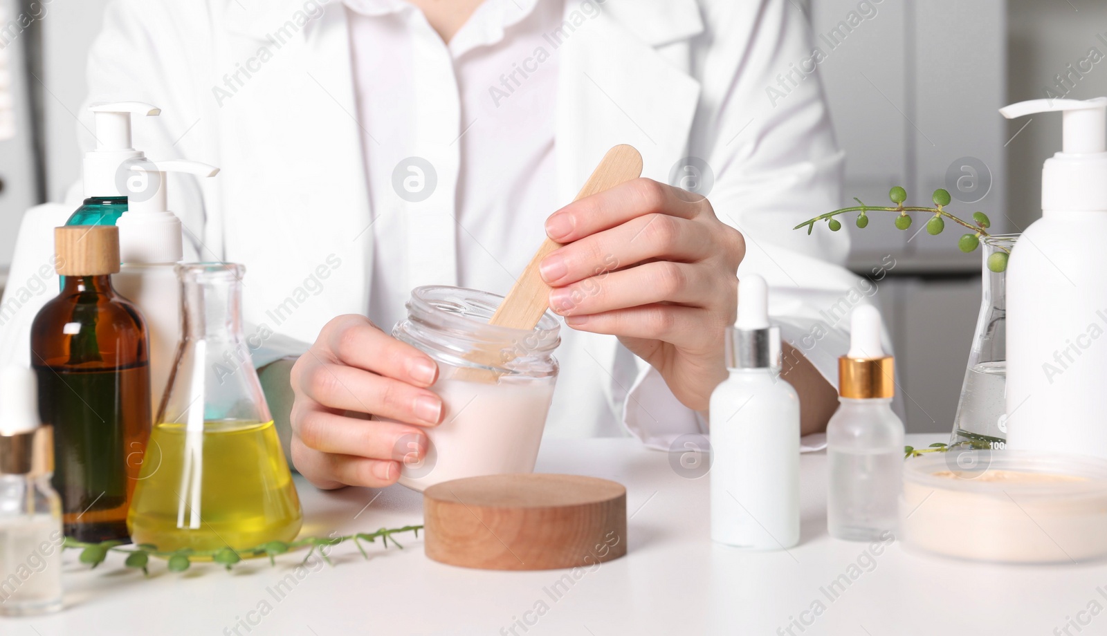 Photo of Dermatologist with jar testing cosmetic product at white table indoors, closeup