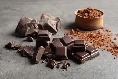 Pieces of chocolate and cocoa powder on grey background