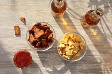 Photo of Different crispy rusks, beer and dip sauce on wooden table, flat lay
