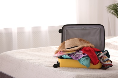 Modern suitcase full of clothes on bed indoors. Space for text