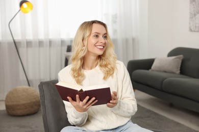 Happy woman in stylish warm sweater reading book at home