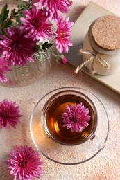 Beautiful chrysanthemum flowers and cup of tea on beige textured table, above view