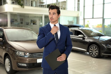 Young salesman with clipboard near car in modern dealership