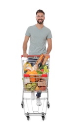 Photo of Happy man with shopping cart full of groceries on white background