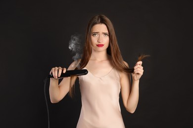 Image of Upset young woman with flattening iron on black background. Hair damage
