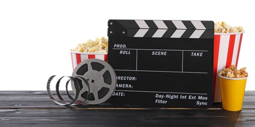 Movie clapper, buckets of tasty popcorn and film reel on wooden table against white background