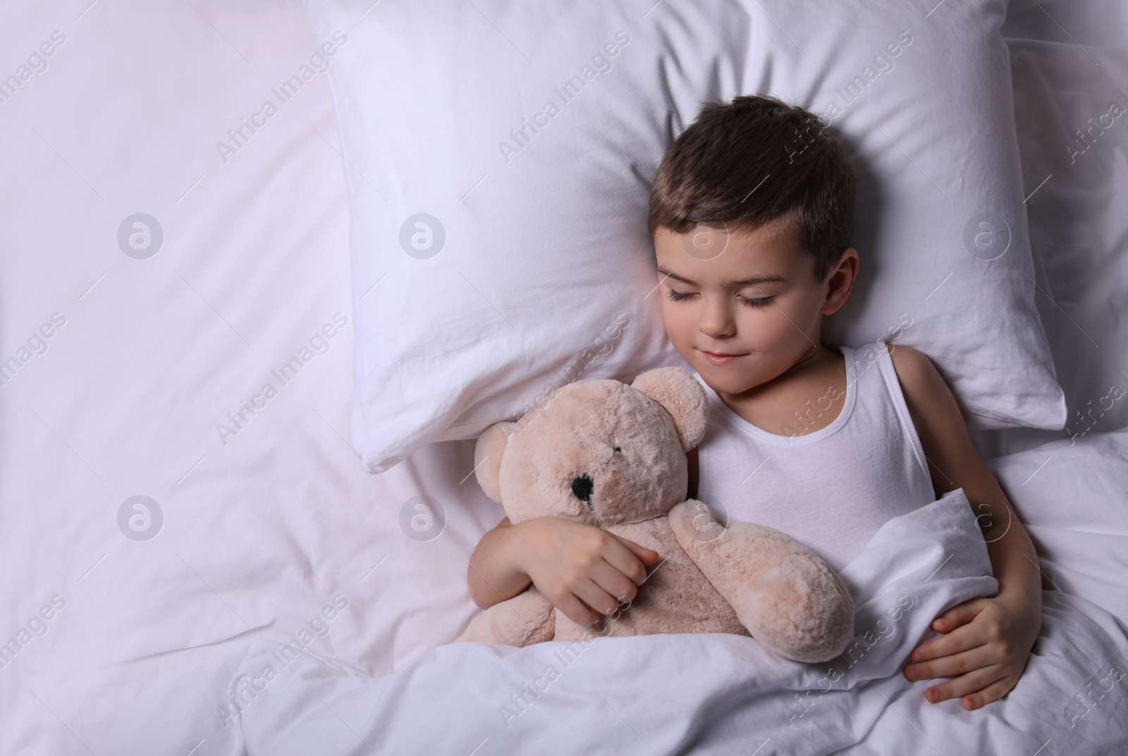 Photo of Little boy sleeping with teddy bear at home, top view. Bedtime