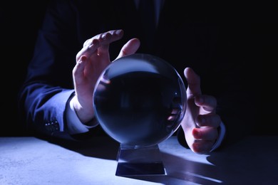 Photo of Businessman using crystal ball to predict future at table in darkness, closeup